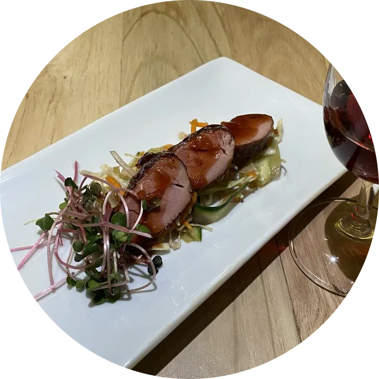 Sliced glazed sausage over microgreens, a glass of red alongside